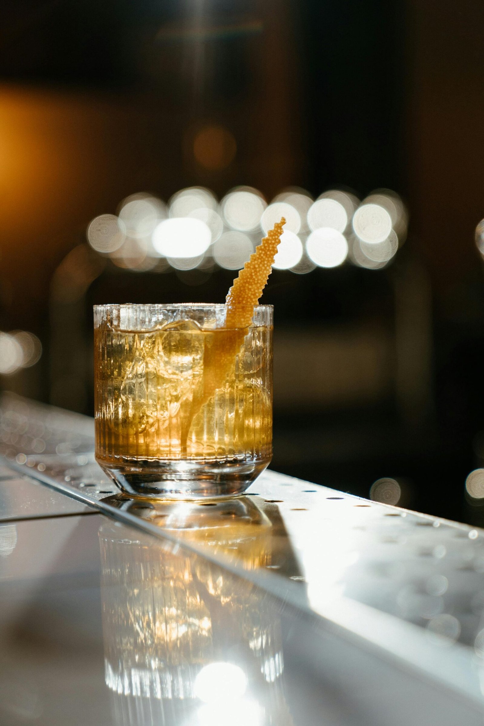 A sophisticated whiskey cocktail with citrus zest garnish and ice cubes, captured at a bar.