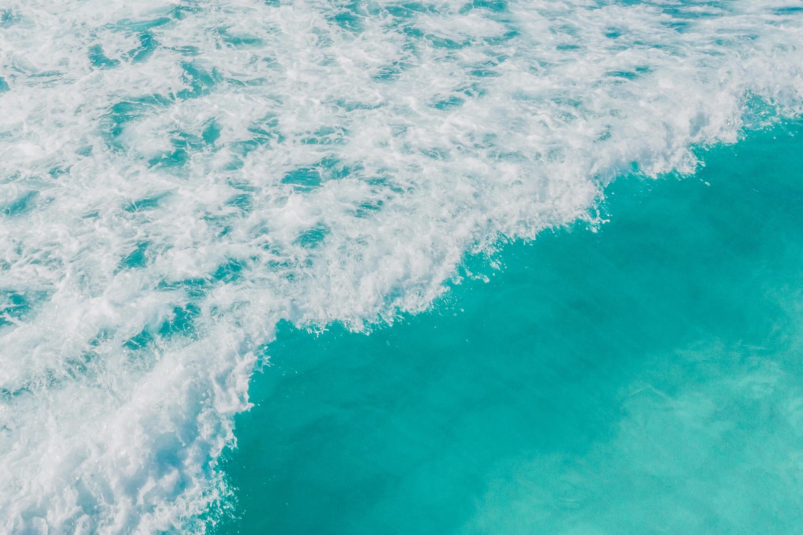 Aerial view of vibrant turquoise ocean waves crashing on the shore, capturing the beauty and energy of the sea.