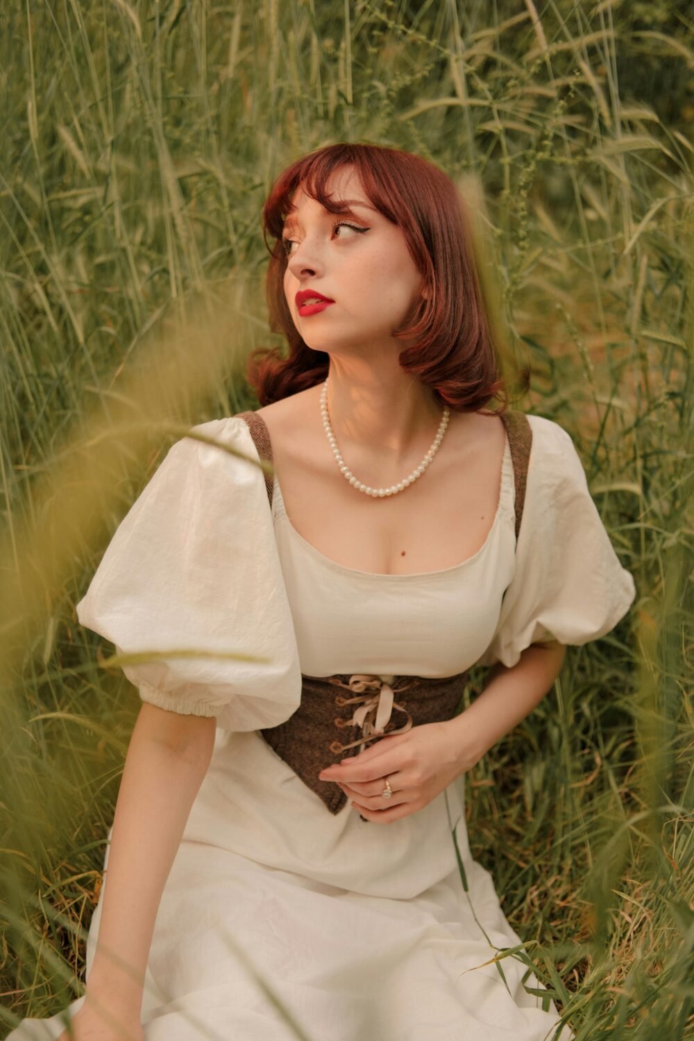 A woman in vintage fashion sits amidst tall grass, evoking a retro style charm.