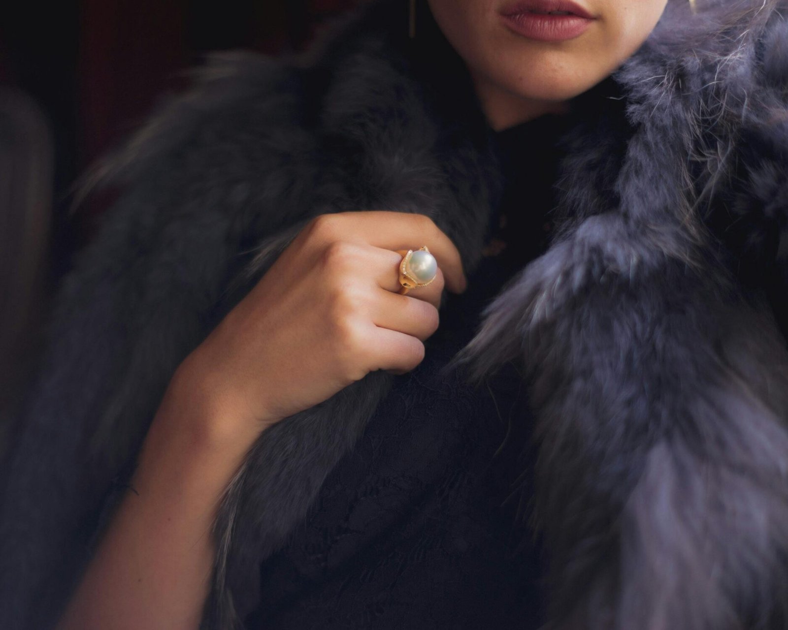 Close-up portrait of a woman draped in fur showing elegance with a pearl ring, perfect for luxury fashion themes.