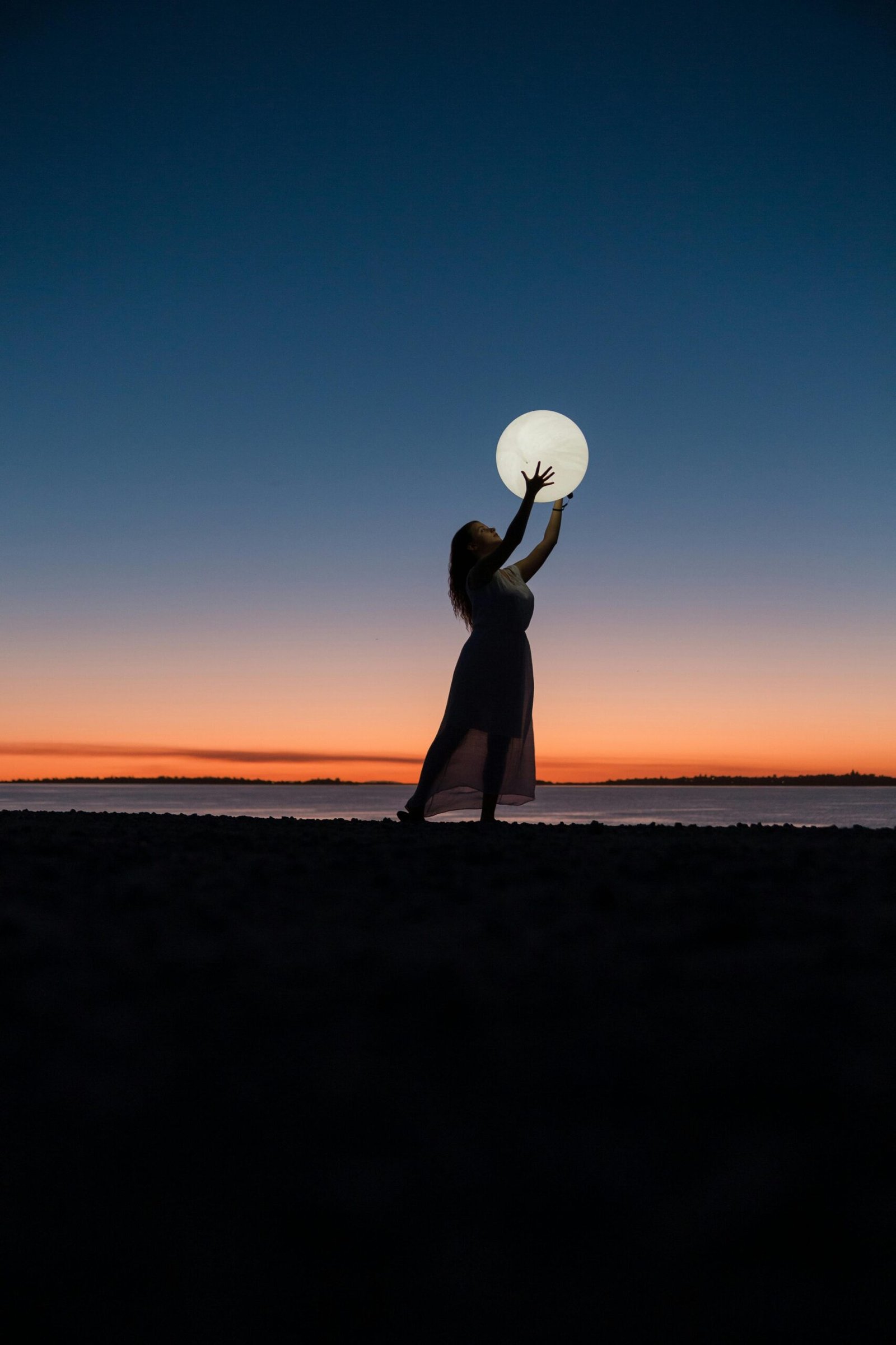 A serene scene of a woman silhouetted against a sunset sky, reaching towards the full moon.