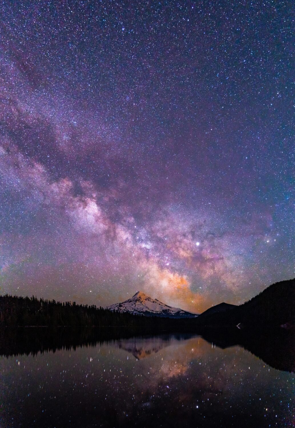 Capture of a brilliant starry night over a serene lake with a mountain peak reflection, creating a magical scene.