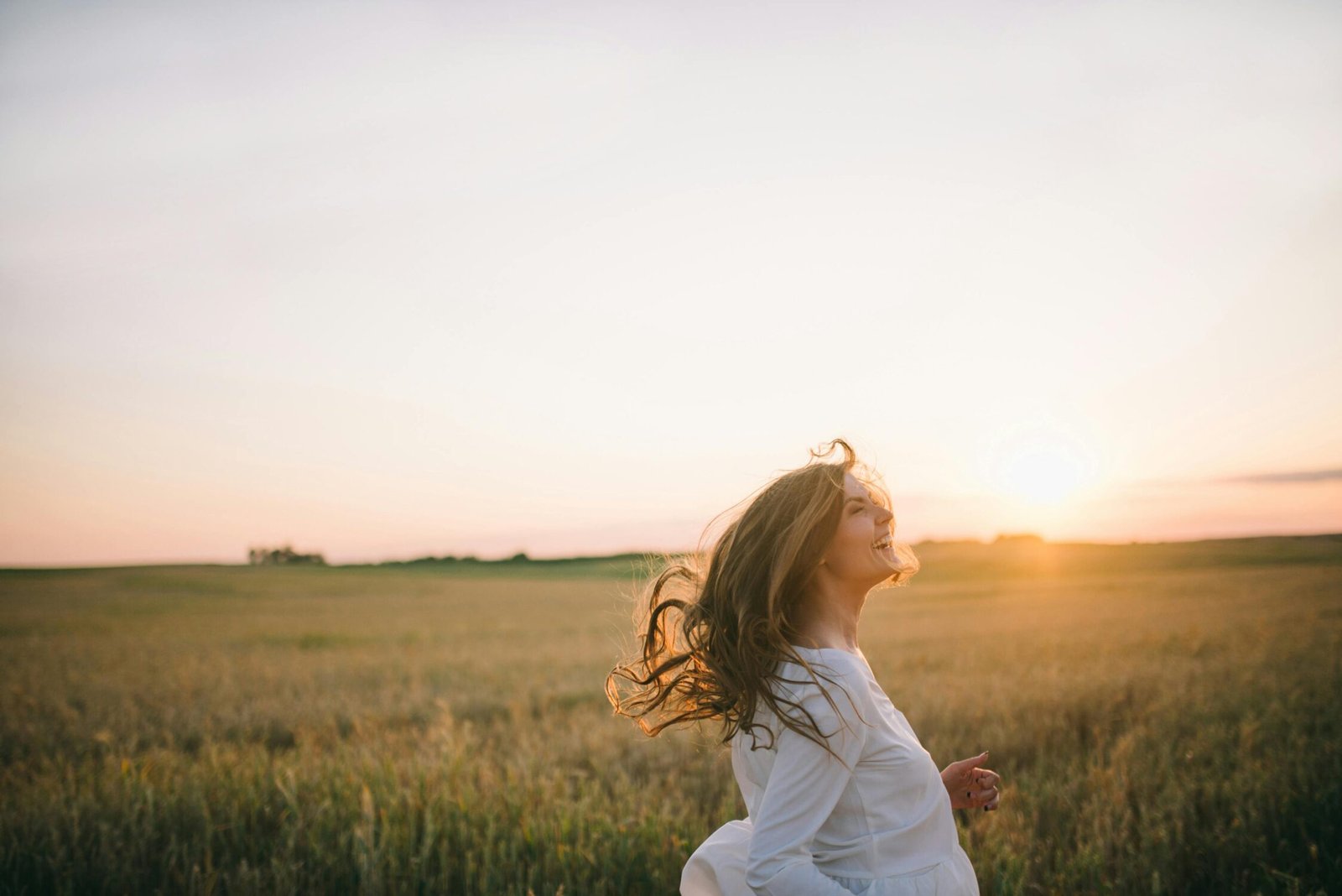 A cheerful woman enjoying a beautiful sunset in a vast wheat field, symbolizing happiness and freedom.